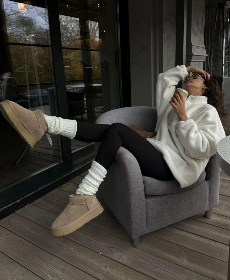Cozy autumn vibes: Relaxing woman in fuzzy sweater, sipping coffee, wearing leggings and boots on a patio chair.