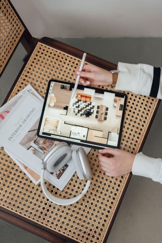 Aesthetics in Design and Artistry Designer using a tablet and stylus for interior planning, with headphones and design magazines nearby on a chair. | Sky Rye Design Designer using a tablet and stylus for interior planning, with headphones and design magazines nearby on a chair.
