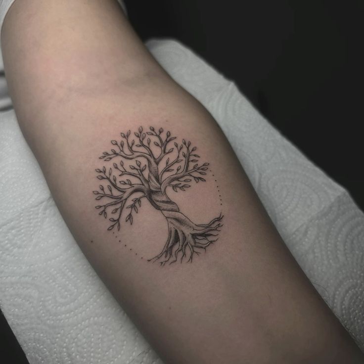 Tree of life tattoo on forearm, depicting intricate branches and roots in black ink.