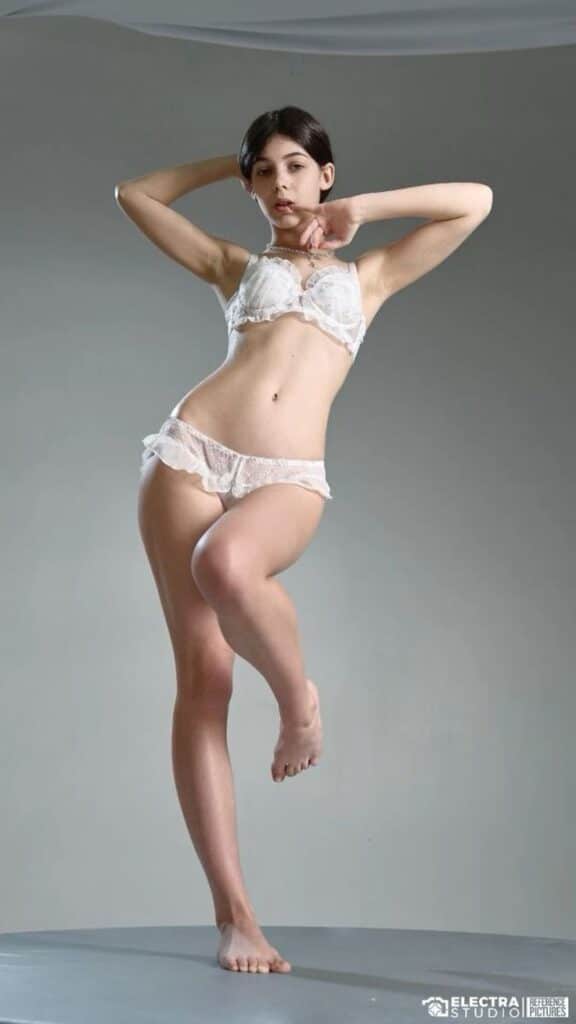 Model posing in white lace lingerie against a gray background, showcasing elegant dance-like posture.
