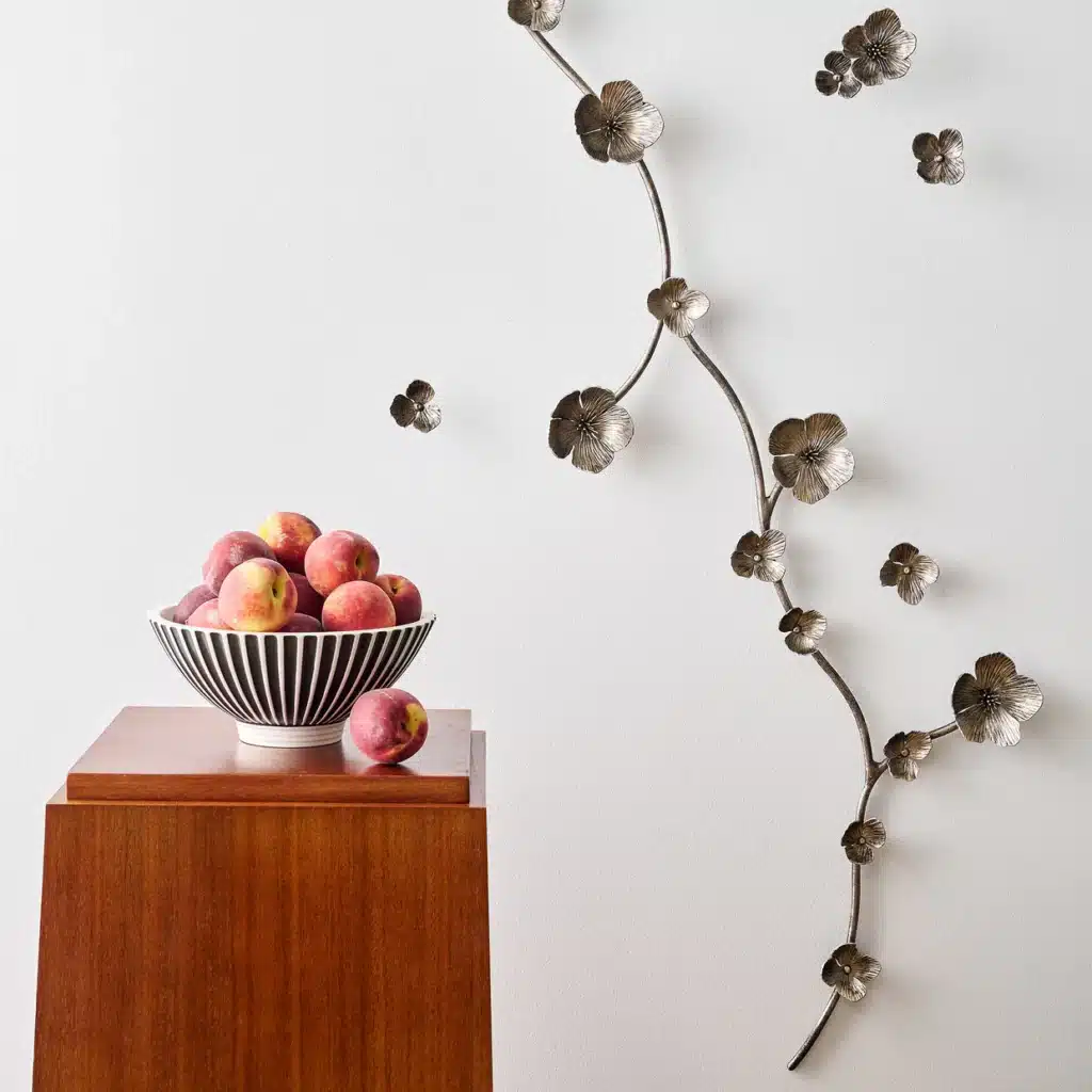 AriaWallSculpture_ClaireCroweCollection-detail2-web Bowl of peaches on wooden stand beside decorative metal floral wall art on a white background. | Sky Rye Design Bowl of peaches on wooden stand beside decorative metal floral wall art on a white background.
