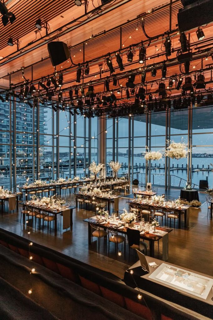 Elegant event venue with scenic waterfront views and beautifully set tables adorned with floral centerpieces.