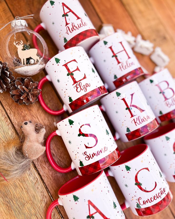 As canecas mais lindas de Natal 🎅 Christmas-themed mugs with names and initials arranged on a wooden table with decorations. | Sky Rye Design Christmas-themed mugs with names and initials arranged on a wooden table with decorations.