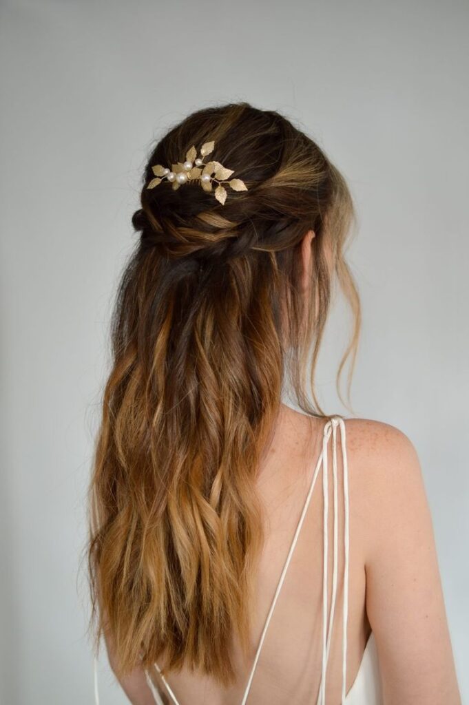 Brunette with a half-up braided hairstyle adorned with a gold leaf hair accessory, wearing a white dress.