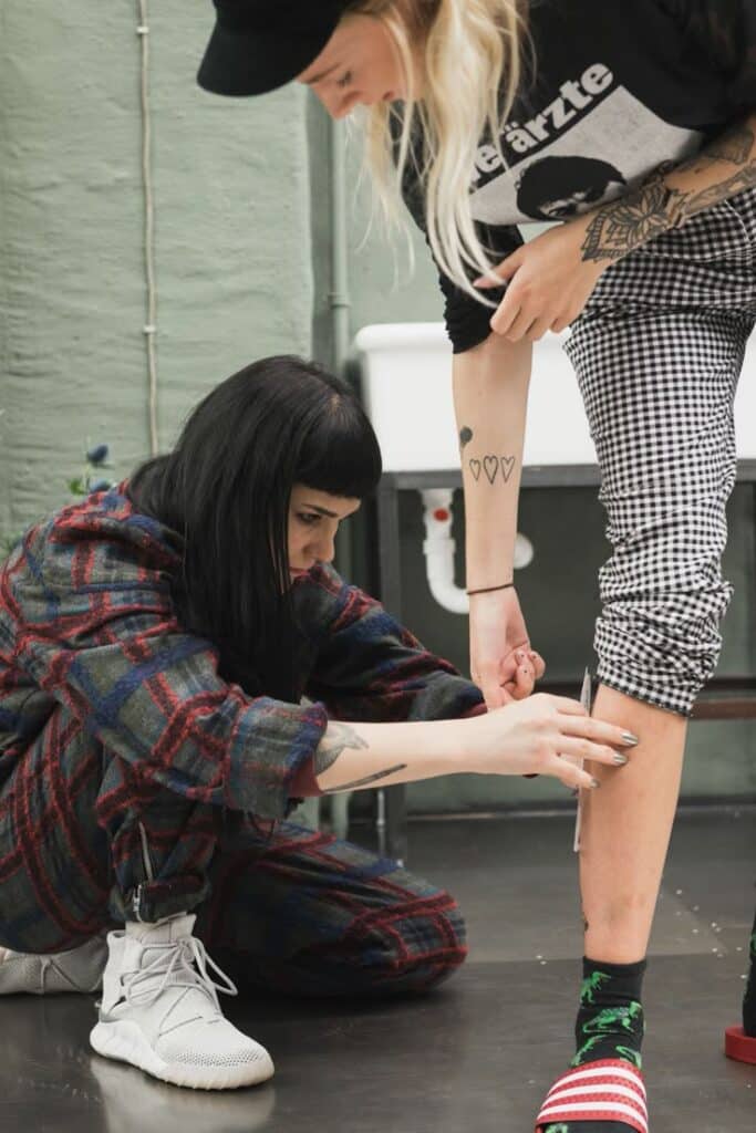 Behind Simone Klimmecks Surreal Tattoo Designs - IGNANT Person kneeling to measure inseam with tape, while another stands in checkered pants. | Sky Rye Design Person kneeling to measure inseam with tape, while another stands in checkered pants.