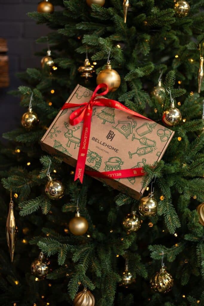 Gift box with red ribbon on a decorated Christmas tree with gold ornaments and lights.