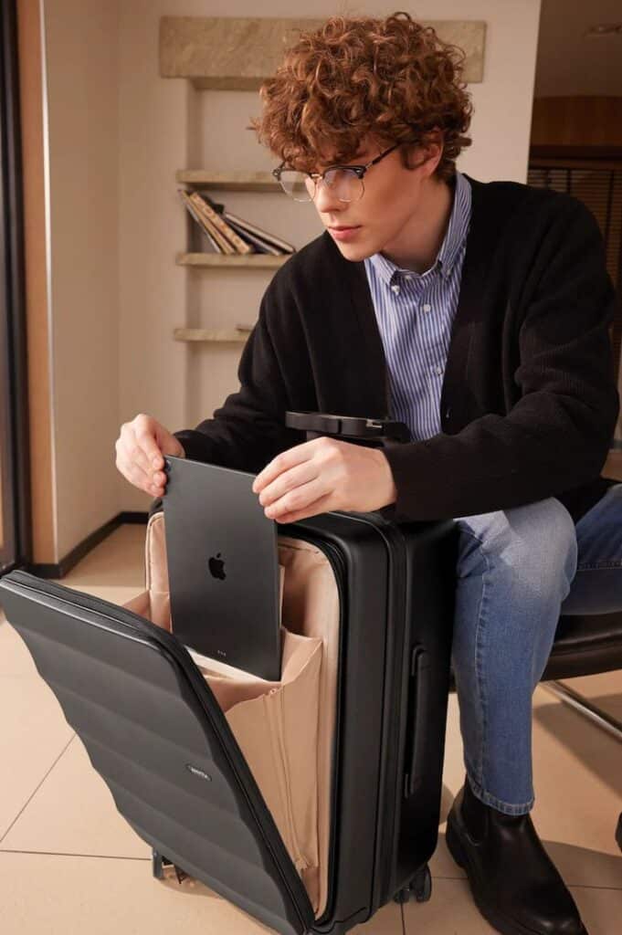 Man packing a tablet into a sleek black suitcase, ready for travel or business trip in stylish indoor setting.