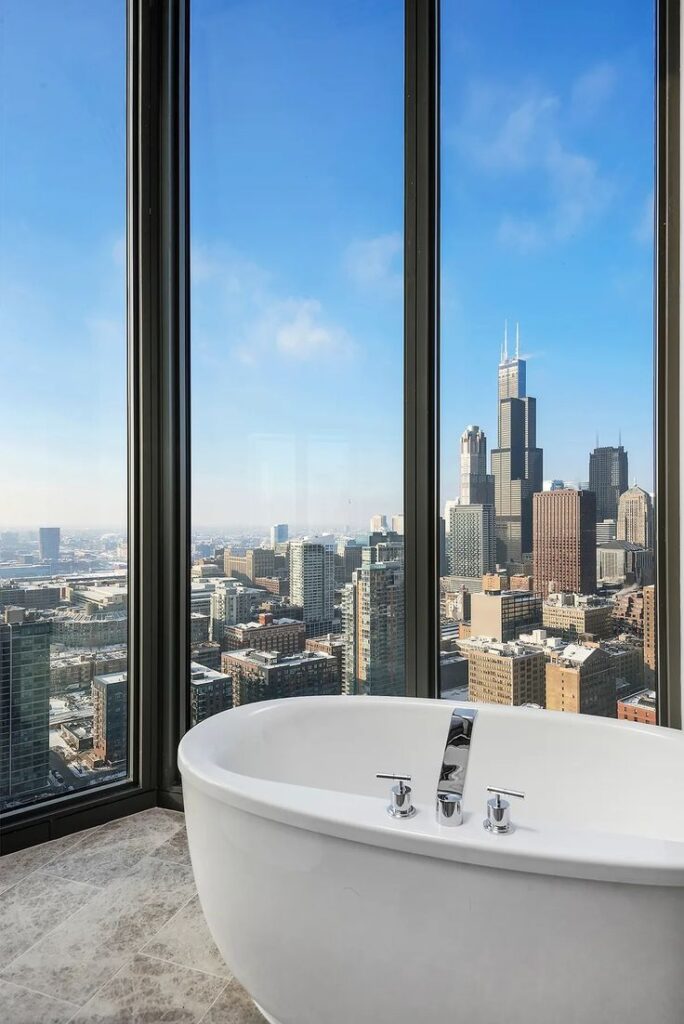 Luxurious bathtub with stunning city skyline view through large windows, featuring iconic Chicago skyscrapers.