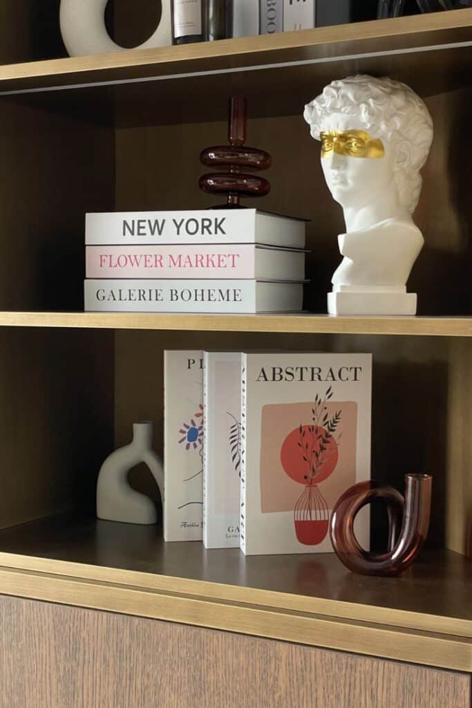 Stylish shelf with art books, abstract decor, and a modern bust in a cozy home library setting.