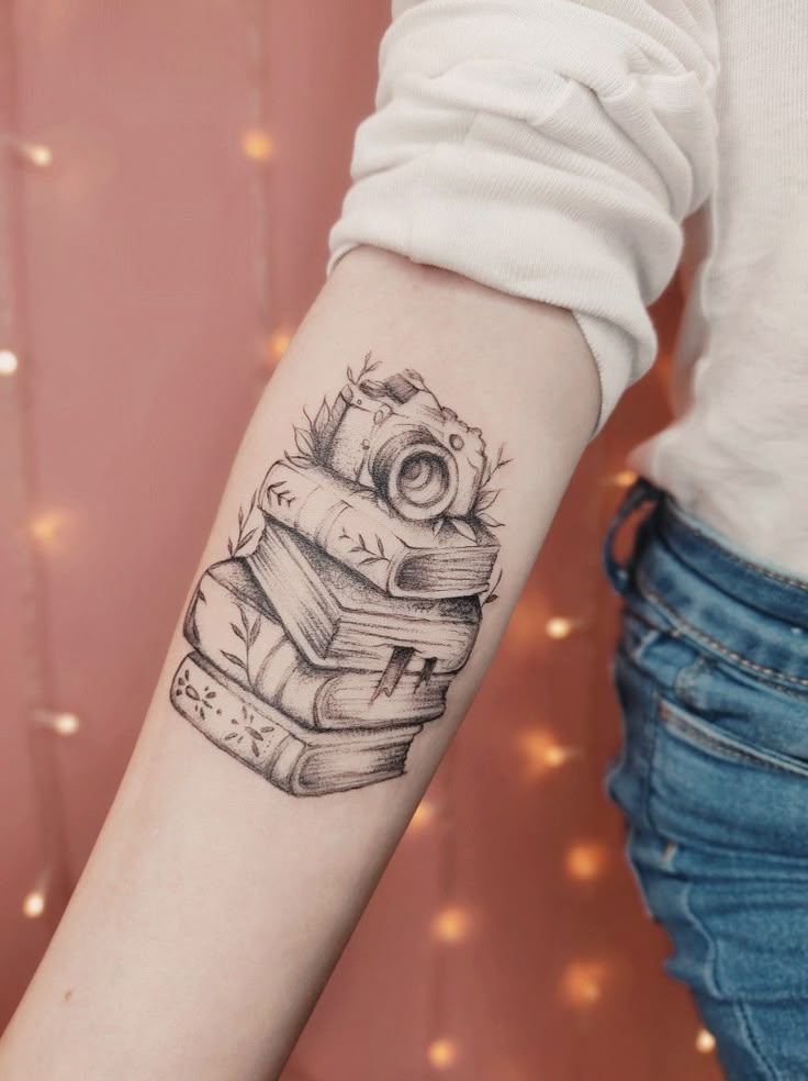 Books and camera tattoo Tattoo of stacked books and vintage camera on forearm, symbolizing photography and literature passion. | Sky Rye Design Tattoo of stacked books and vintage camera on forearm, symbolizing photography and literature passion.