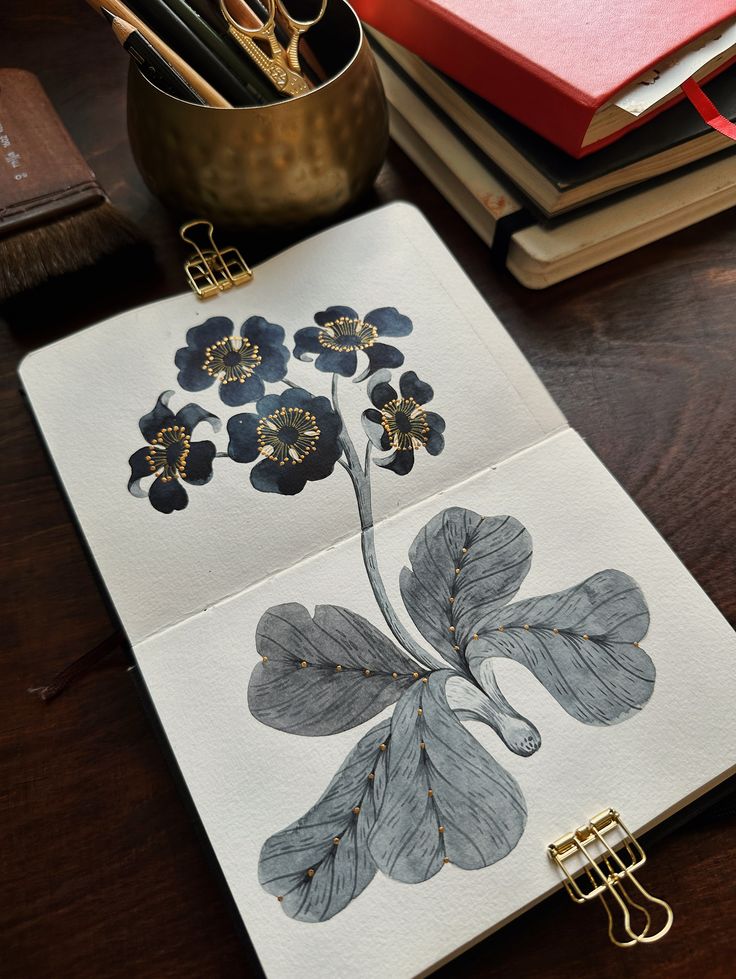 Artistic black floral illustration in an open sketchbook on a wooden desk with stationery and books.