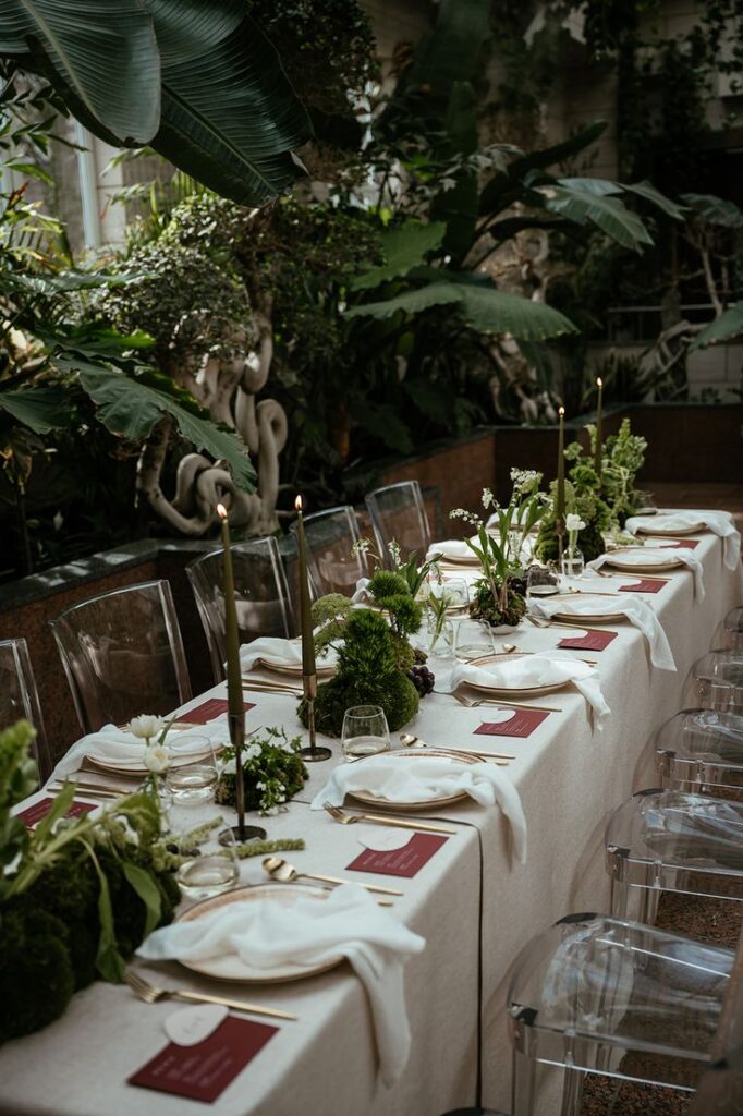 Elegant banquet table in lush garden, adorned with candles, greenery, and clear chairs. Perfect for a nature-themed event.