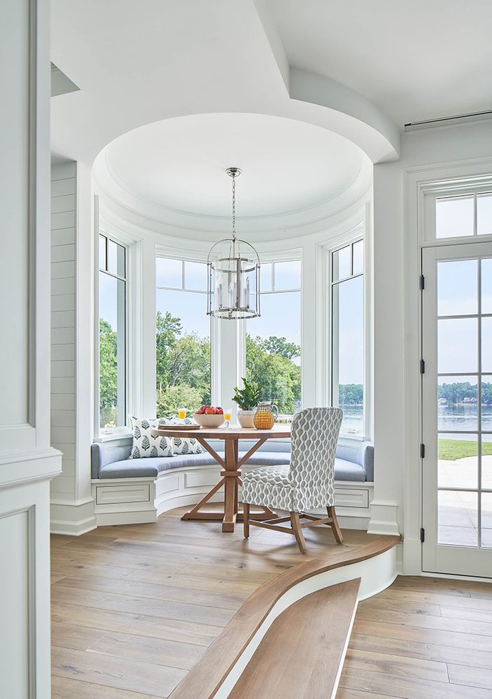 Elegant breakfast nook with round table and bay windows overlooking a serene lakeside view.