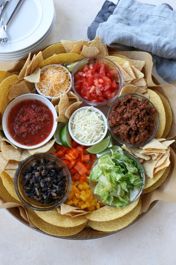 A vibrant nacho platter with salsa, cheese, ground meat, veggies, and tortillas, perfect for a hearty appetizer spread.