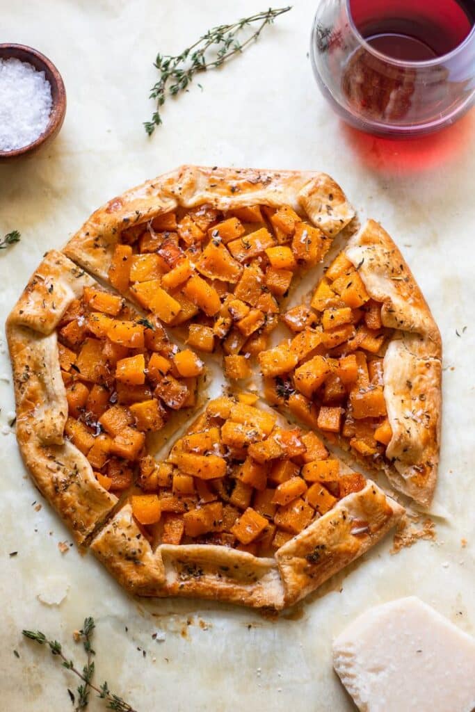 Butternut Squash Galette Rustic butternut squash galette with thyme and a glass of red wine on parchment paper. | Sky Rye Design Rustic butternut squash galette with thyme and a glass of red wine on parchment paper.