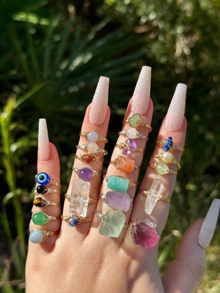Hand with long nails showcasing colorful gemstone rings in sunlight. Perfect for jewelry fashion inspiration.