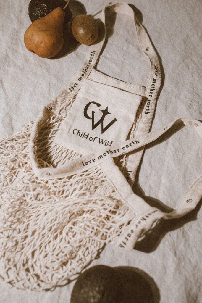 Eco-friendly reuseable cotton mesh bags with Child of Wild logo, surrounded by fruits on a linen surface.