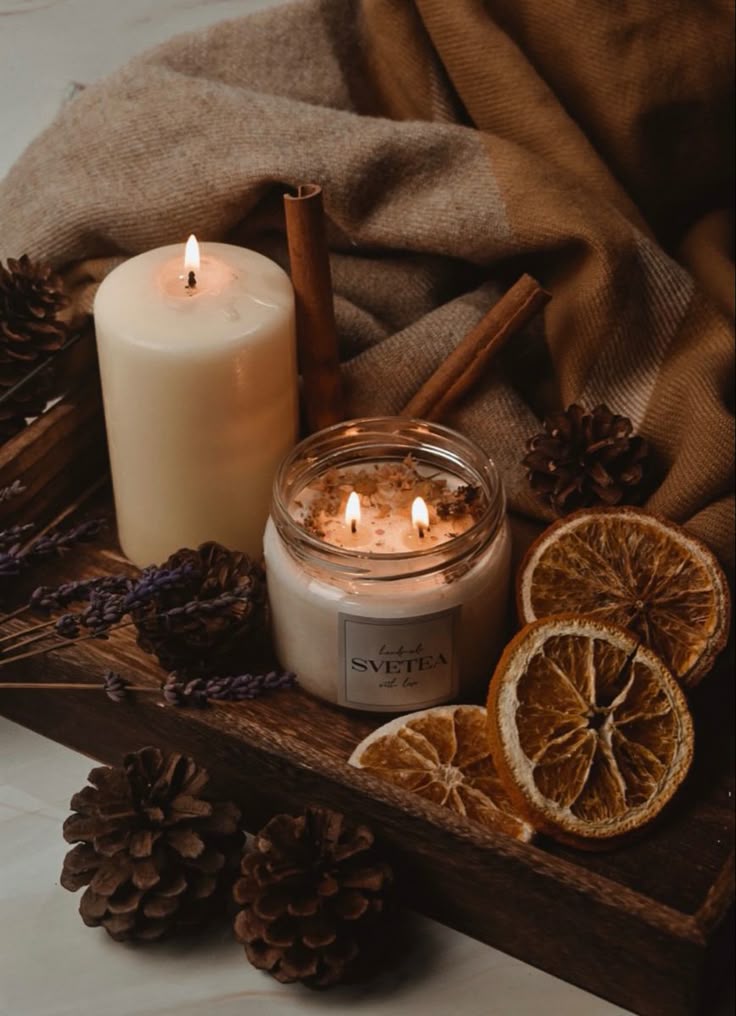 Cozy candlelit setting with jar and pillar candles, dried oranges, pinecones, and cinnamon sticks on a wooden tray.
