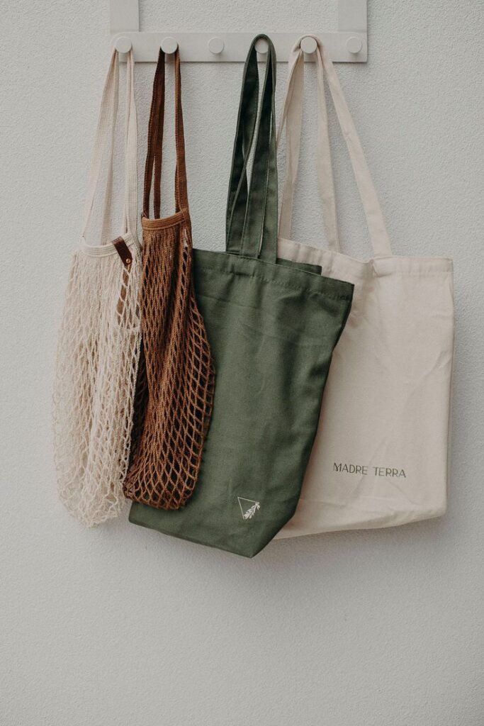 Eco-friendly reusable bags hanging on hooks, featuring mesh and canvas designs in earthy tones.