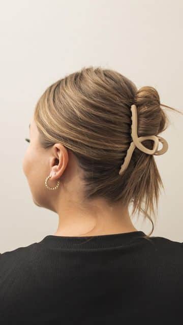 Woman with blonde hair styled in an updo, secured with a beige hair clip, wearing a black top and hoop earring.