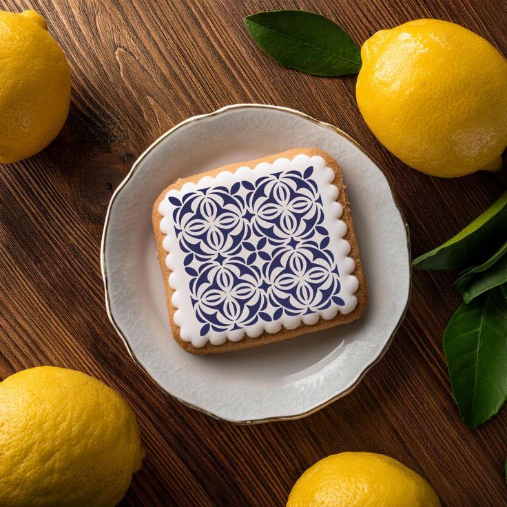 Decorative cookie with blue patterned icing, surrounded by fresh lemons on wooden table.
