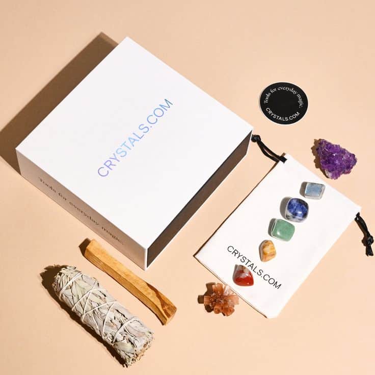 Crystal kit with sage, stones, Palo Santo, and branded box from Crystals.com on a beige background.
