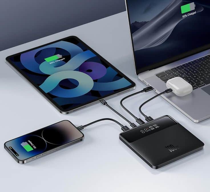 Multiple devices charging via a black power bank: tablet, smartphone, laptop, and wireless earbuds connected simultaneously.