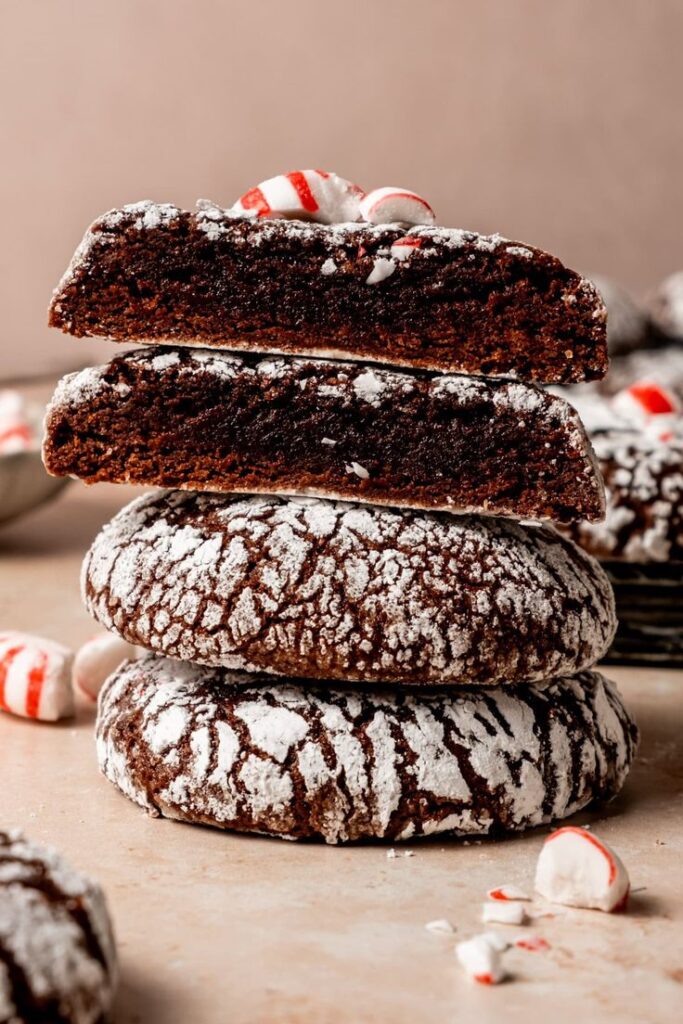 Stack of chocolate crinkle cookies dusted with powdered sugar, topped with peppermint candy pieces. Perfect holiday treat!