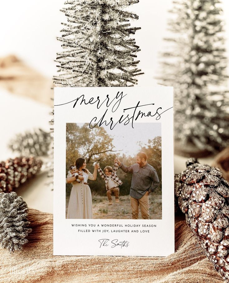 Family holiday card with Merry Christmas text, photo of parents and child, festive winter decor with pinecones and trees.