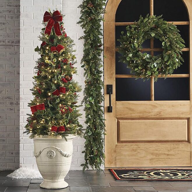 Christmas Cheer 5 ft_ Pre-Lit Potted Tree with Pine Cones Red Berries Festive entryway with decorated Christmas tree, garland, and wreath on wooden door. Holiday décor inspiration. | Sky Rye Design Festive entryway with decorated Christmas tree, garland, and wreath on wooden door. Holiday décor inspiration.