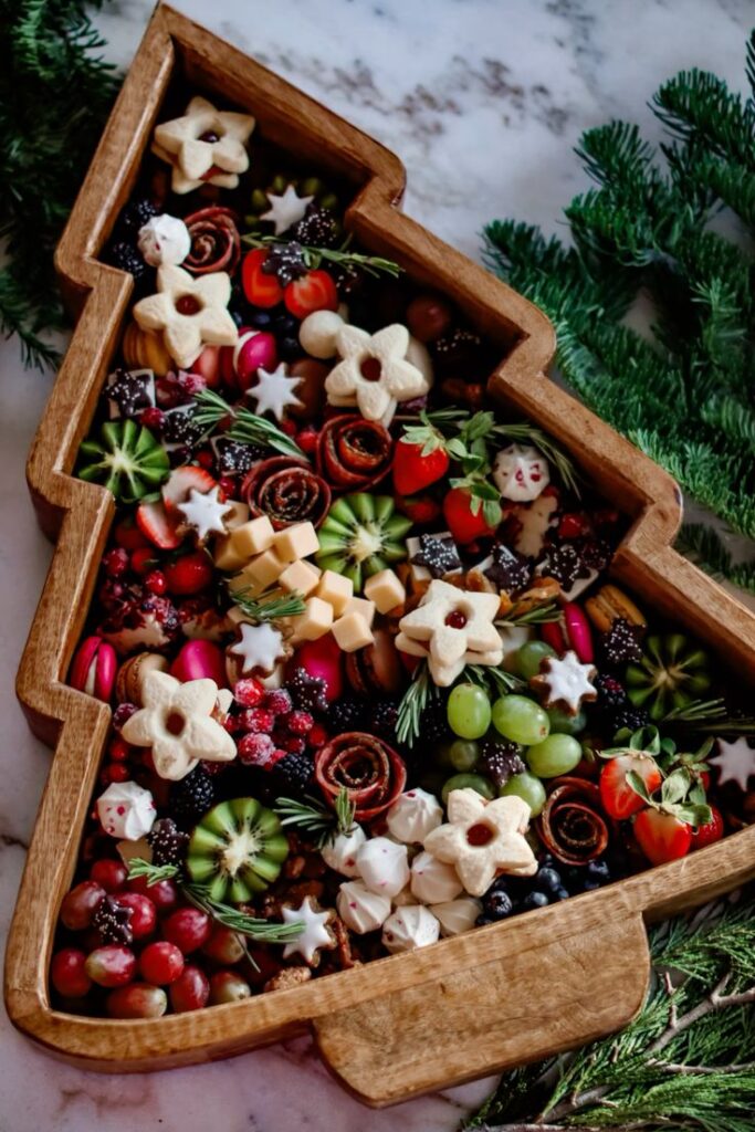 Holiday-themed charcuterie board with festive cookies, fruits, and cheeses in a tree-shaped wooden tray. Christmas dinner