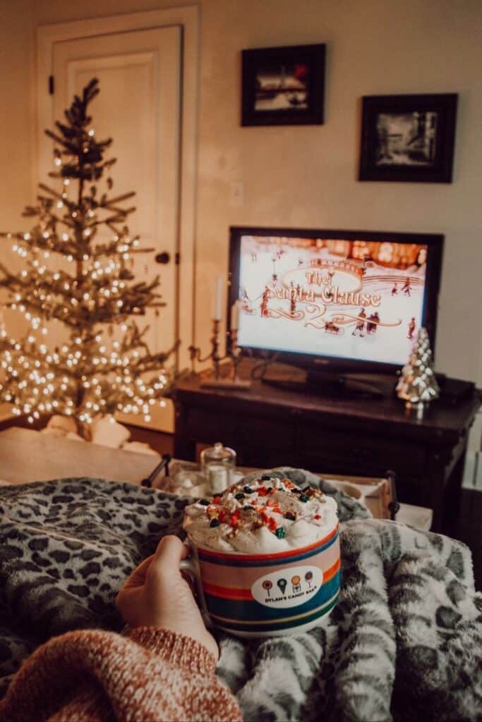 Cozy Christmas scene with hot cocoa, a lit tree, and festive movie on TV, perfect for a winter night at home. Christmas movies