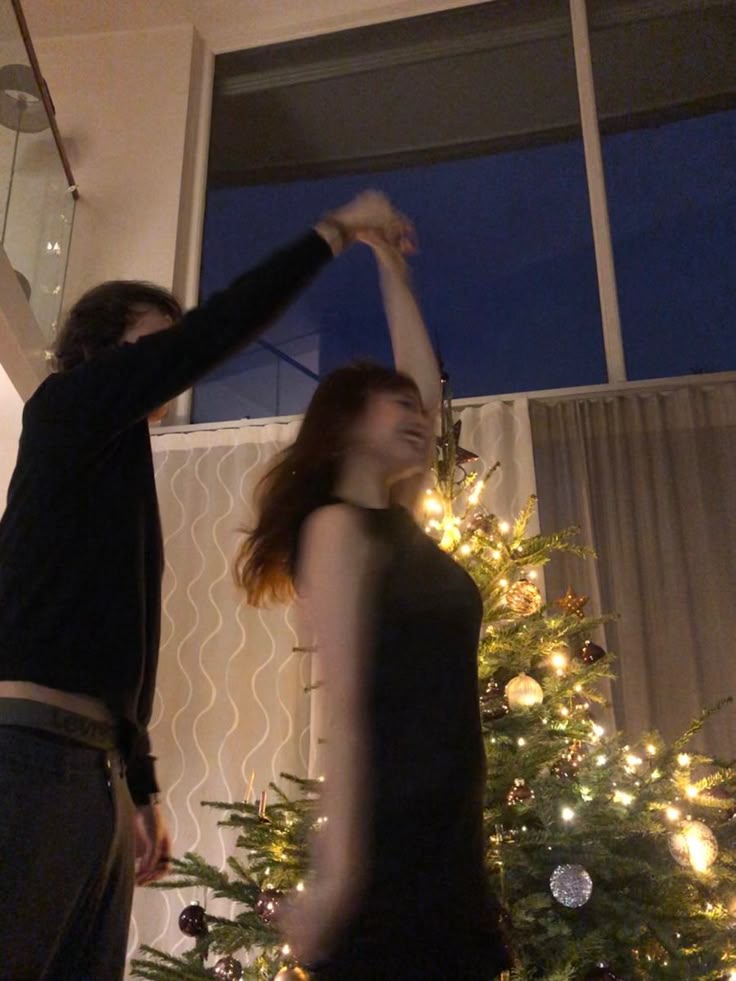 Couple dancing by Christmas tree, warm festive holiday vibes with twinkling lights.