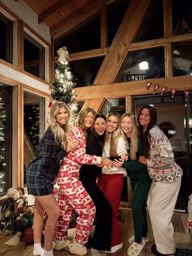 Christmas era ☃️❤️🪵 Group of friends in cozy pajamas posing by a decorated Christmas tree in a wooden cabin, smiling and celebrating together. | Sky Rye Design Group of friends in cozy pajamas posing by a decorated Christmas tree in a wooden cabin, smiling and celebrating together.