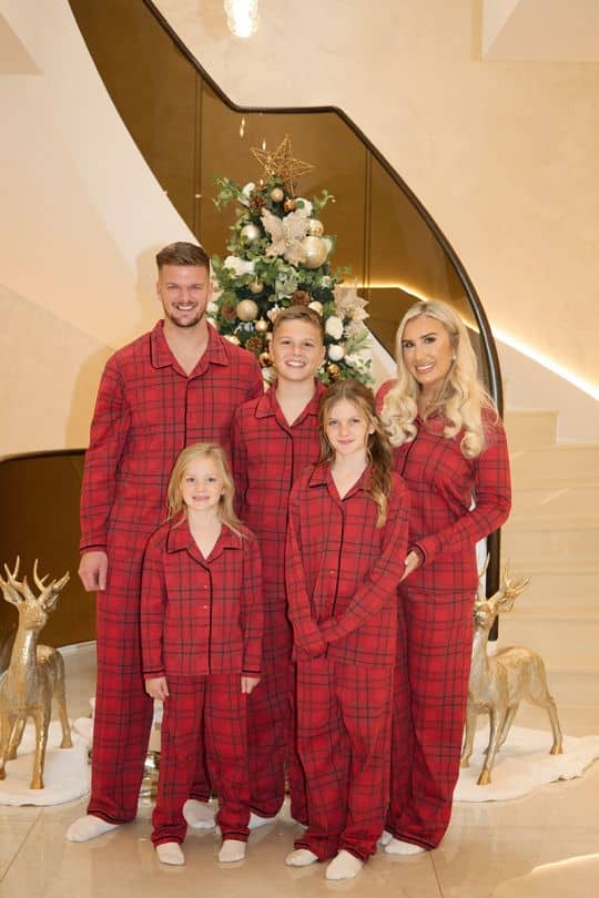 Family in matching red pajamas pose by a decorated Christmas tree with golden reindeer ornaments.