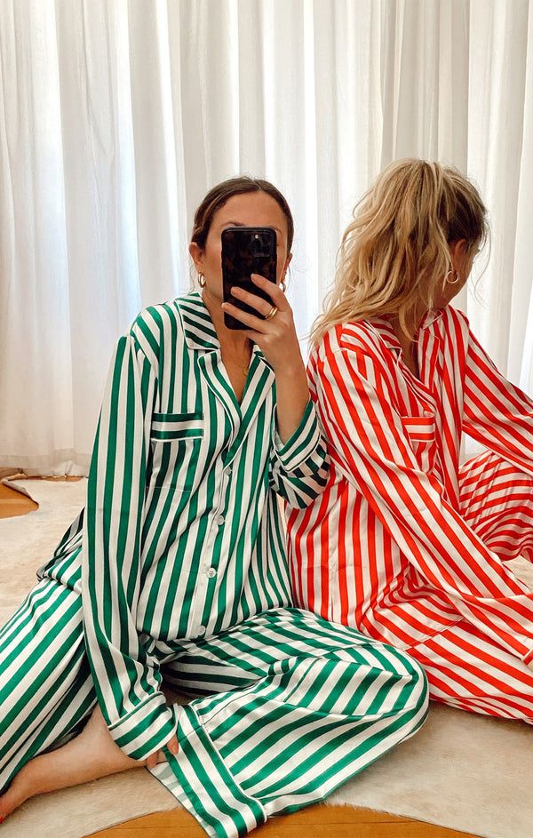 Classic PJ Set Two people in stylish striped pajamas, green and red, sitting on the floor by white curtains, one taking a selfie. | Sky Rye Design Two people in stylish striped pajamas, green and red, sitting on the floor by white curtains, one taking a selfie.