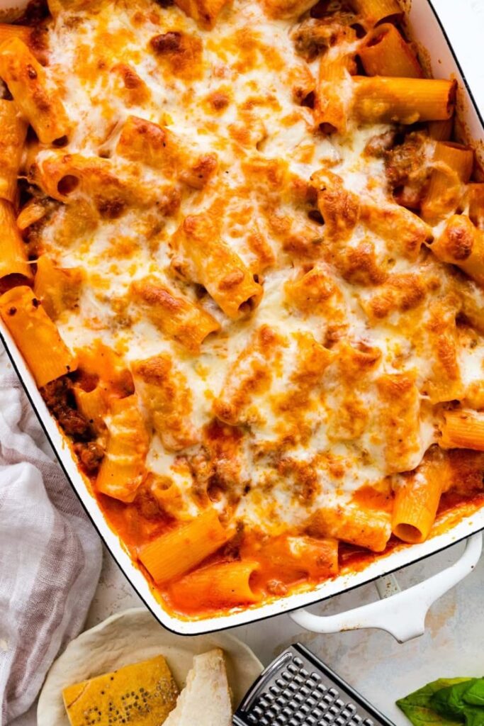 Cheesy baked rigatoni pasta in a white dish with browned cheese and tomato sauce, topped with mozzarella.