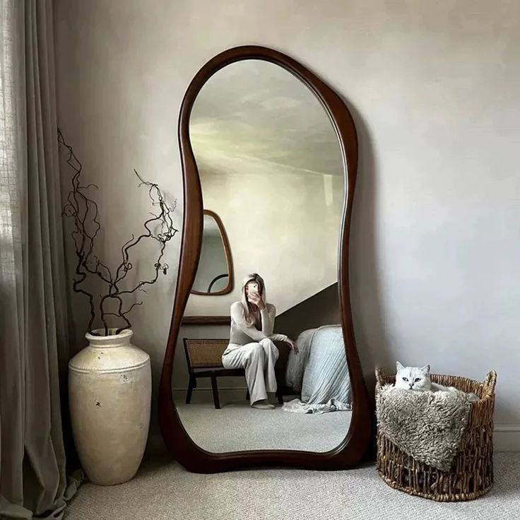 Cozy room with large mirror, woman sitting, cat in basket, and decorative vase.