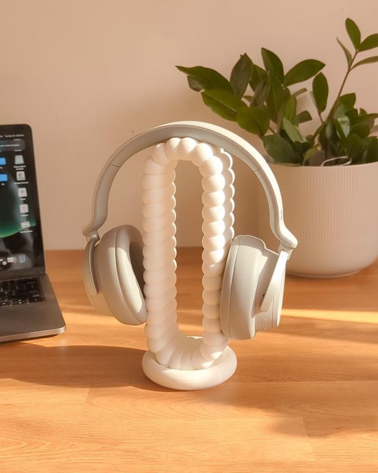 Gray headphones on a unique spiral stand on a wooden desk, plant in background, natural light highlights the setup.