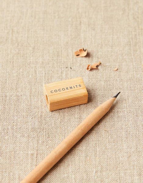 Cocoknits Recycled Paper Pencils Wooden pencil sharpener and pencil on textured fabric with shavings, labeled Cocoknits for eco-friendly writing tools. | Sky Rye Design Wooden pencil sharpener and pencil on textured fabric with shavings, labeled Cocoknits for eco-friendly writing tools.