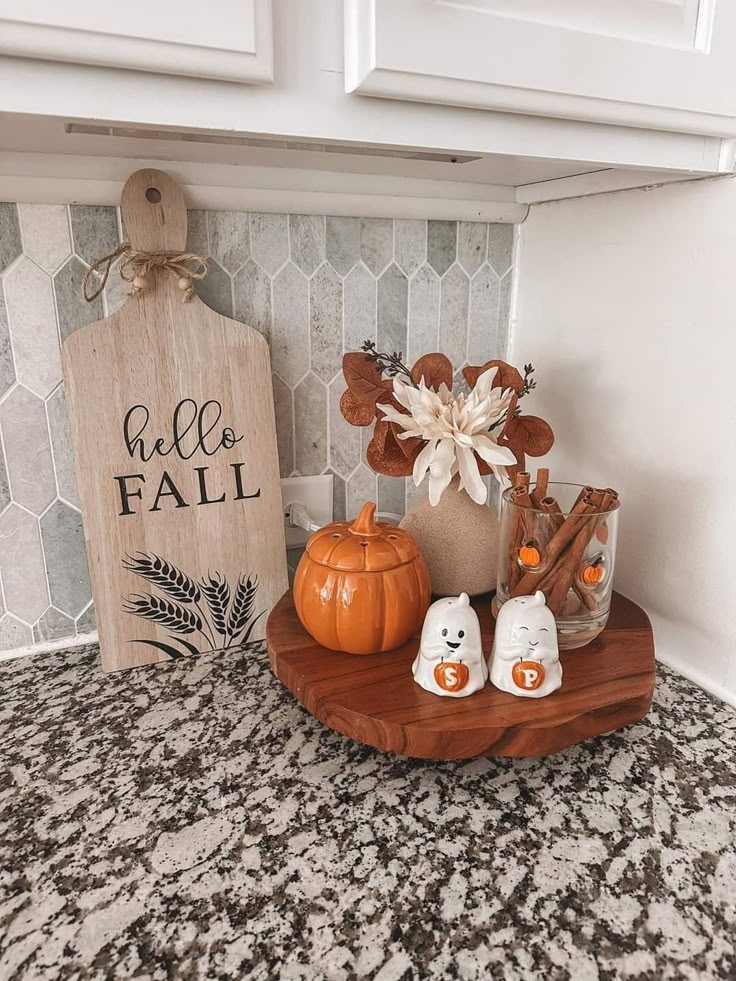 Festive fall kitchen decor with a pumpkin jar, spice shakers, cinnamon sticks, and a Hello Fall sign on granite countertop.