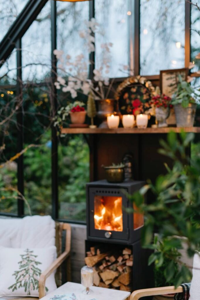 Cozy indoor setting with a burning stove, candles, and festive decorations in a greenhouse during winter.