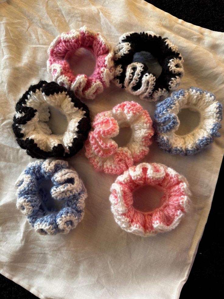 Crochet Scrunchies_ Handmade Hair Accessory Colorful handmade crochet scrunchies arranged on a white cloth, showcasing various patterns and colors. | Sky Rye Design Colorful handmade crochet scrunchies arranged on a white cloth, showcasing various patterns and colors.