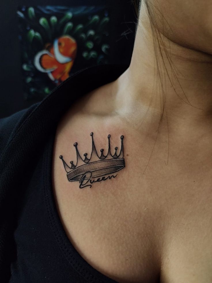 Crown tattoo Crown tattoo with queen text on upper chest, behind an orange fish artwork. Elegant and bold body art design. | Sky Rye Design Crown tattoo with queen text on upper chest, behind an orange fish artwork. Elegant and bold body art design.