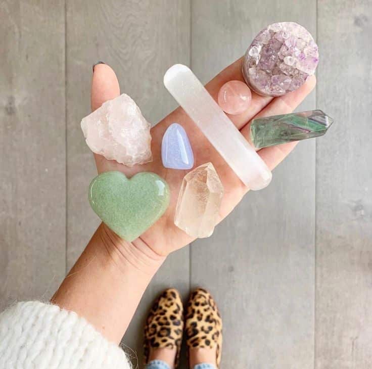 Hand holding various colorful healing crystals on wooden floor background, showcasing crystal collection.