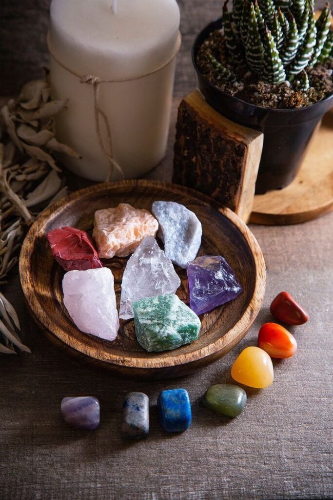 Colorful healing crystals and smooth stones in a wooden dish with candle and plant for spiritual wellness.