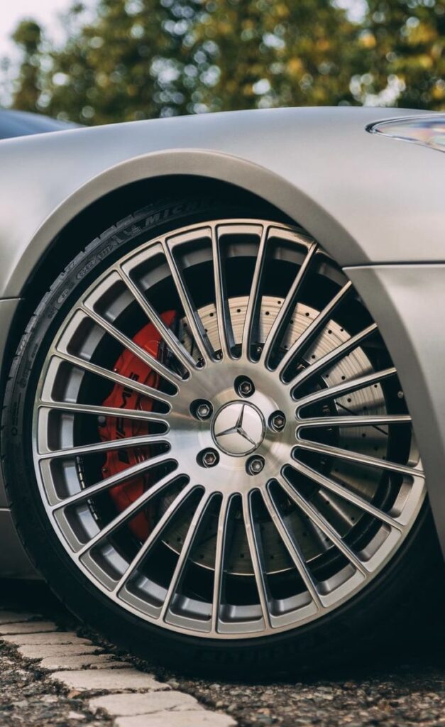 Close-up of a silver Mercedes-Benz car wheel and red brake caliper, highlighting vehicle engineering and luxury design.