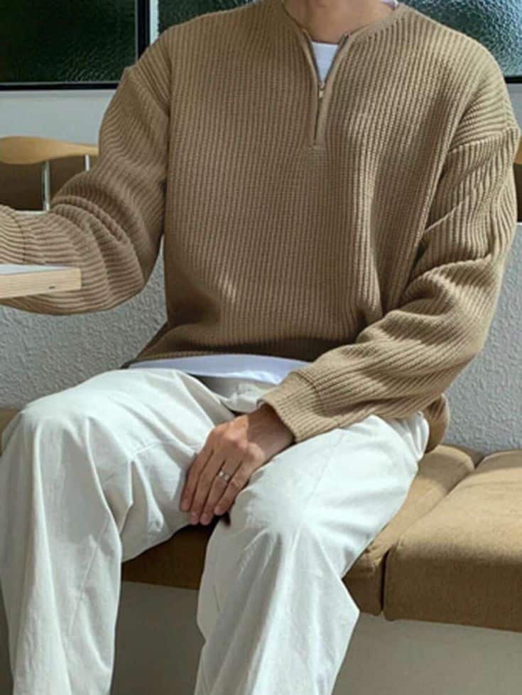 DAZY Men Half Zip Drop Shoulder Sweater Man in a cozy brown sweater and white pants sitting on a bench, exuding a casual and relaxed style. | Sky Rye Design Man in a cozy brown sweater and white pants sitting on a bench, exuding a casual and relaxed style.