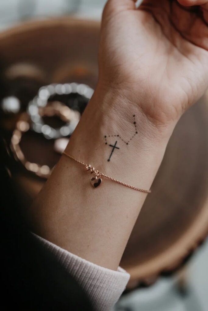 Delicate Small Cross Wrist Tattoo Ideas for Women Wrist tattoo of constellation with cross; rose gold bracelet with heart charm adds elegance. | Sky Rye Design Wrist tattoo of constellation with cross; rose gold bracelet with heart charm adds elegance.