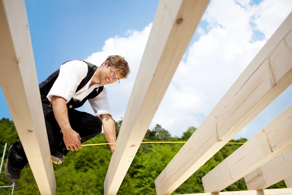Worker measuring wooden beams outdoors under blue sky.